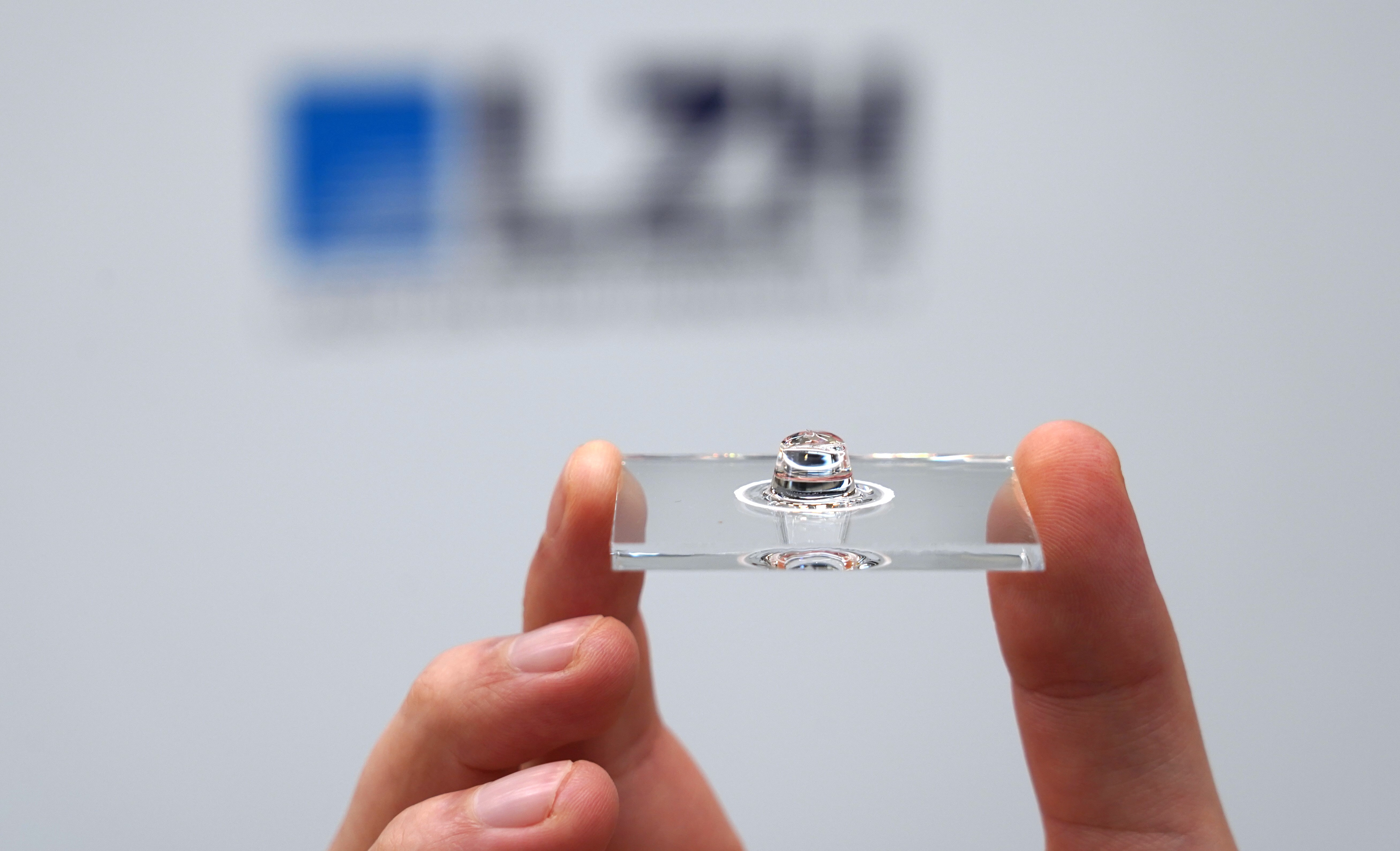 Glasscheibe mit sphärischer Linse, die von zwei Fingern gehalten wird.