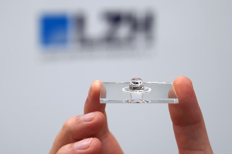 Glasscheibe mit sphärischer Linse, die von zwei Fingern gehalten wird.