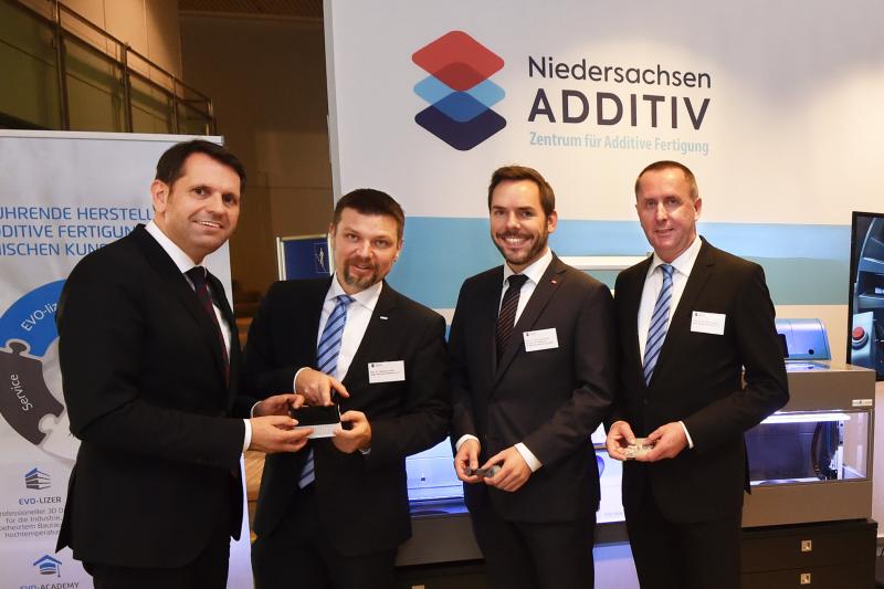 LZH Executive Director Dr. Dietmar Kracht presents an additively manufactured safety cap for a fuse box in automobiles to Lower Saxony's Minister of Economics, Labour and Transport Olaf Lies (f.l.t.r.: Olaf Lies, Dr. Dietmar Kracht (LZH), Dr.-Ing. Malte Stonis (IPH) and Dr.-Ing. Stefan Kaierle (LZH)). (Photo: Ralf Büchler)