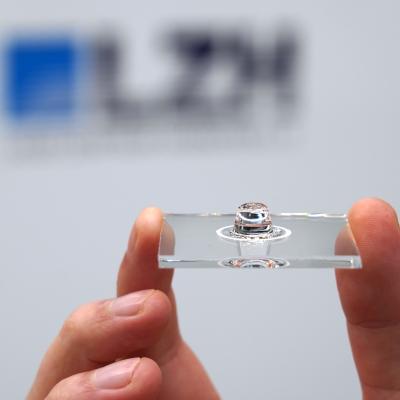 Glasscheibe mit sphärischer Linse, die von zwei Fingern gehalten wird.